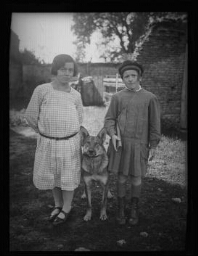 Portrait en pied d'une jeune fille et d'un jeune écolier dehors avec un chien Berger allemand entre eux, Louvagny le 6 octobre 1929