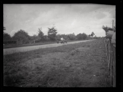 Le Mans (Sarthe) : circuit des 24 heures : voiture sur le circuit ; main d'un spectateur tenant un papier derrière une palissade en bois au premier plan