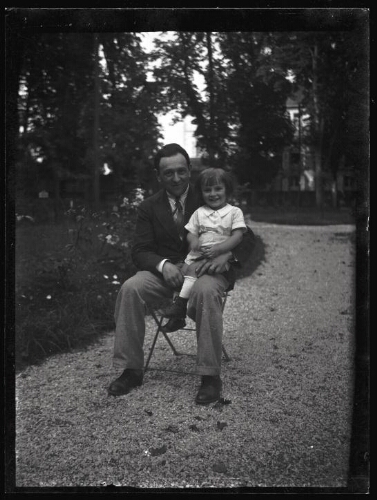 Portrait en pied d'un homme assis dehors sur une chaise de jardin avec une fillette sur ses genoux