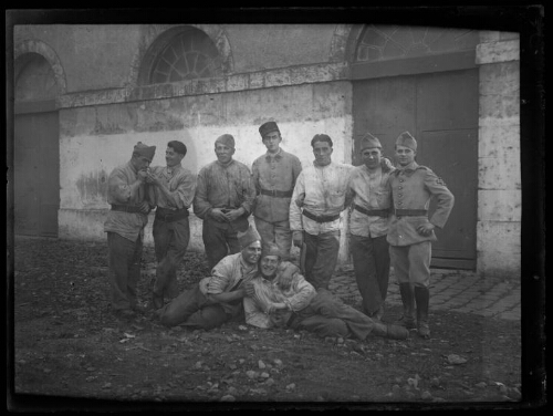 Militaires : neuf hommes en habit militaire posent devant une vieille bâtisse ; deux d'entre eux sont assis par terre devant les autres ; l'homme au centre porte un képi du 401e régiment d'artillerie anti-aériens