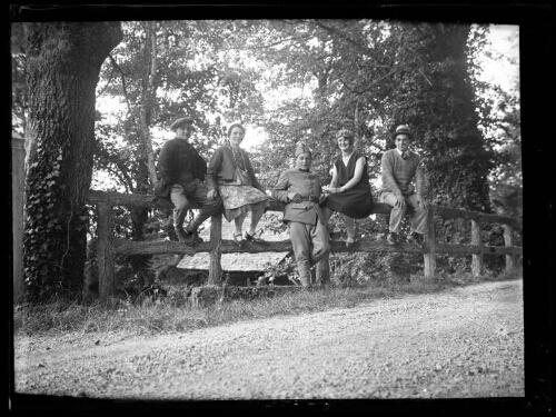 Groupe de personnes : deux couples assis sur une clôture en bois au bord d'une route avec un militaire debout entre eux
