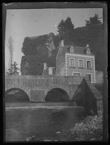 Fresnay-sur-Sarthe (Sarthe) : pont du Creusot qui enjambe La Sarthe où passe l'avenue Victor Hugo ; homme en habit militaire à l'angle du pont ; vestiges du château recouvert de végatation en arrière-plan