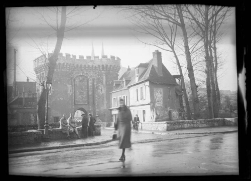 Chartres (Eure et Loire) : La porte Guillaume construite sur l'emplacement d'un ancien donjon ; deux militaires sont assis sur un muret près d'un groupe de trois personnes debout de dos ; une femme traverse la chaussée et un homme avec son vélo traverse le pont ; une des maisons derrière la porte Guillaume porte l'enseigne "Tabac", une autre porte l'enseigne publicitaire "Amieux Frères"