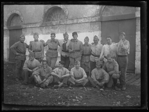 Militaires : quinze hommes en habit militaire posent alignés devant une vieille bâtisse ; l'homme au centre debout porte un képi du 401e régiment d'artillerie anti-aériens