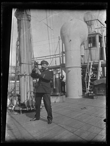 Homme en habit de marin, sur un bateau, au pied du mat, regardant dans un sextant