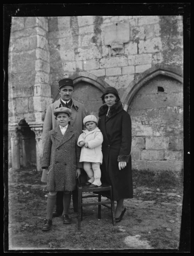 Portrait d'une famille devant un monument ; un couple et deux enfants sont debout dehors ; l'homme porte un képi du 401e régiment d'artillerie anti-aériens ; le jeune enfant se tient debout sur une chaise