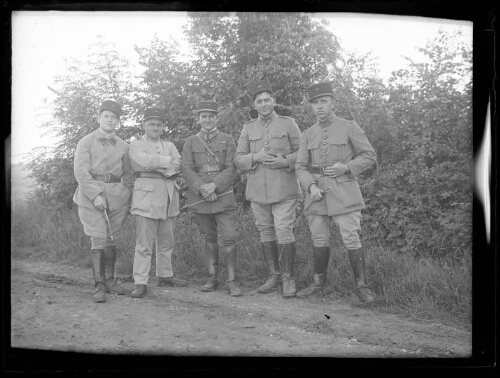 Militaires : cinq hommes en habit militaire posent debout sur le bord d'un chemin ; tous portent un képi du 401e régiment d'artillerie anti-aériens et trois d'entre eux tiennent une baguette de bois dans leur main ; arbustes en arrière-plan
