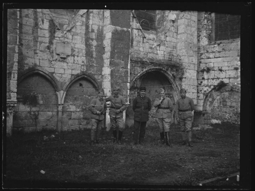 Militaires : cinq hommes en habit militaire alignés debout devant une vieille bâtisse ; l'homme au centre porte un képi du 401e régiment d'artillerie anti-aériens