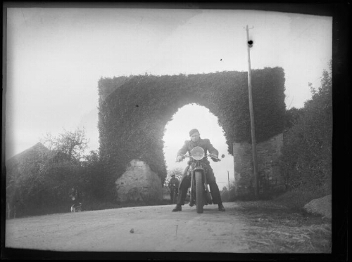 Bourg-le-Roi (Sarthe) : Deux hommes à moto sous la porte fortifiée du village