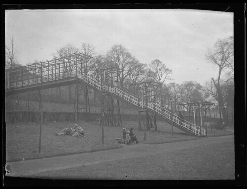 Paysage : immense escalier construit sur pilotis avec quatre militaires assis sous l'escalier et une femmes avec deux enfants assis sur un banc