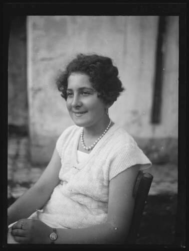 Portrait en buste d'une jeune femme aux cheveux courts assise de trois quart sur une chaise dehors