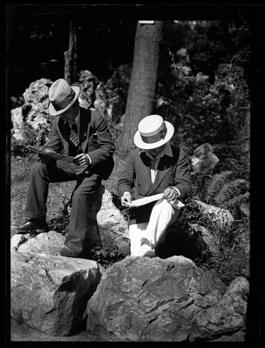 Marc Bry et l'un de ses amis lisent le journal, assis sur des rochers dans un parc