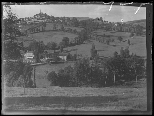 Paysage de campagne : paysage vallonné où les parcelles de terrain sont délimitées par des arbres ; village en arrière-plan en haut d'une butte