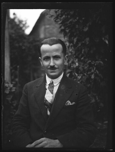 Portrait en buste d'un homme moustachu, vêtu d'une veste à pochette, d'une chemise à rayure et d'une cravate imprimée