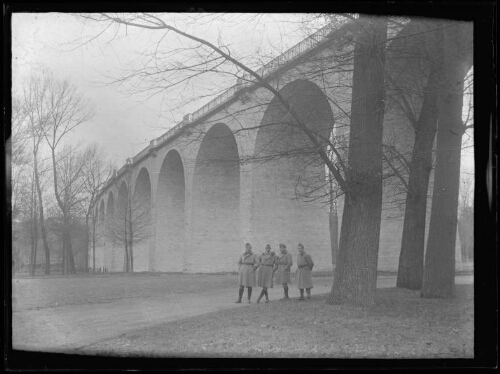 Chartres (Eure-et-Loir) : viaduc de Chartres ; quatre militaires posent debout au pied d'un viaduc où passe une route ; arbres en contrebas du viaduc