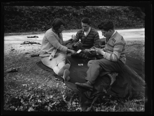 Marc Bry avec Robert Desloges et sa femme, assis dehors sur une couverture près d'une route, jouent aux cartes 