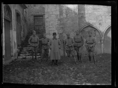 Militaires : six hommes en habit militaire alignés debout devant une vieille bâtisse ; l'homme au centre porte un manteau et un képi du 401e régiment d'artillerie anti-aériens