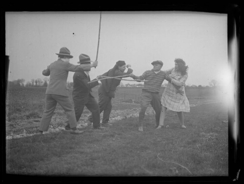 Scène de lutte : une femme et quatre hommes se battent avec des batons dans un champ ; la femme est protégée par l'un des hommes