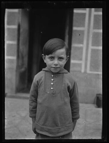 Portrait, en buste, d'un jeune garçon devant une maison