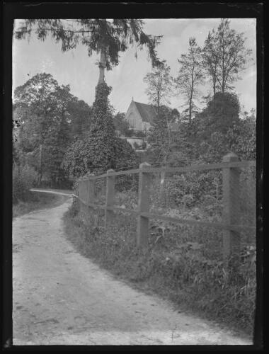 Essay (Orne) : la chapelle des Ducs d'Alençon en arrière plan de la route longeant une barrière, le 18 août 1929