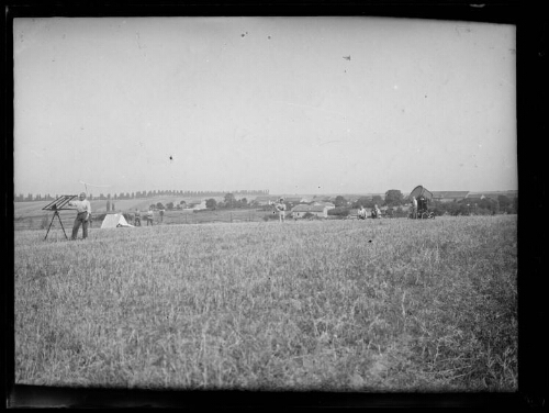 Militaires dans un champ ; l'un d'eux est debout près d'une antenne de réception radio ; projecteur pour l'atterrissage des avions et maisons en arrière-plan