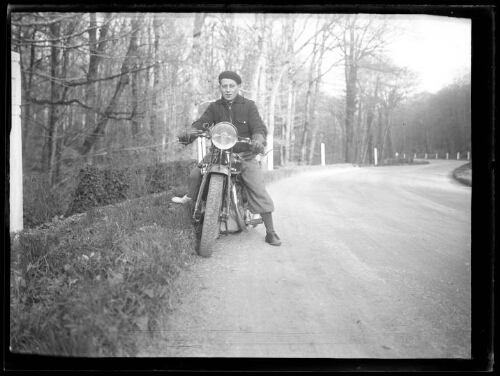 Marc Bry sur sa moto (marque Peugeot) à l'arrêt au bord d'une route sinueuse en forêt, le 19 mars 1936