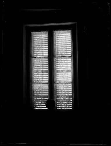 Alençon (Orne) : fenêtre aux rideaux brodés de fleurs et aux volets persiennes fermés ; un globe terrestre est posé sur un guéridon devant la fenêtre