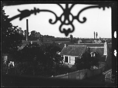 Alençon (Orne) ? : jardins et maisons ; en arrière-plan, la cheminée d'une usine ; ferrures ouvragées d'un balcon au premier plan