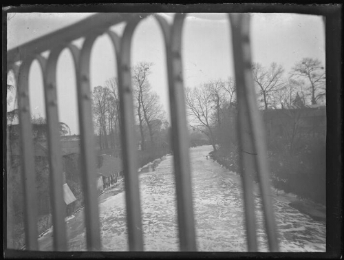 Lavoir et maisons au bord d'une rivière ; photo prise à travers les grilles d'un pont ?