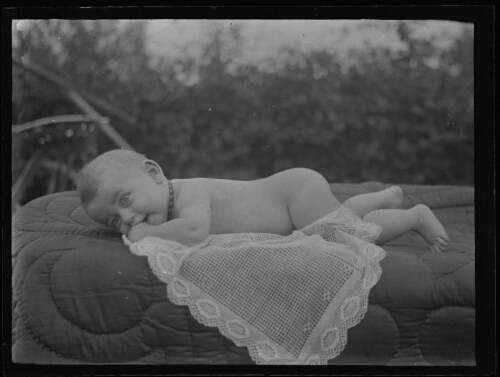 Nourrisson nu allongé sur le ventre sur un édredon dehors, septembre 1929